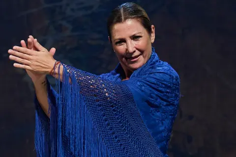 Sara Baras, joven y vibrante, luce un mantón azul eléctrico con flecos, sus manos en un gesto flamenco.