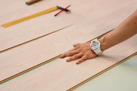 Mano con orologio bianco posata su pannelli di parquet chiaro, pronti per essere tagliati.