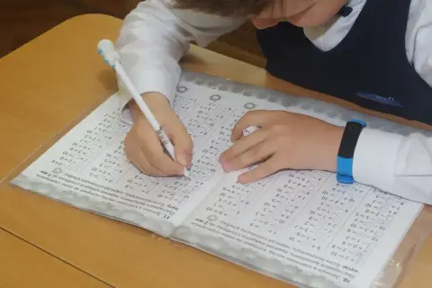 Dziecko pisze długopisem po karcie z zadaniami matematycznymi.