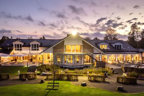 Abendstimmung am Golfclub Heckenhof. Beleuchtetes Clubhaus mit Terrassen und Gartenanlage im Dämmerlicht.