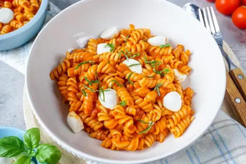 Eine Schüssel mit köstlicher One Pot Pasta, Fusilli in Tomatensauce mit Mozzarella-Kugeln und frischem Basilikum garniert.