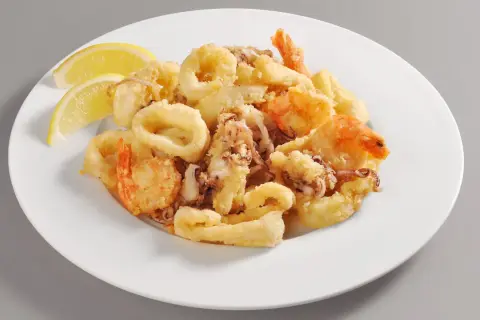 Un invitante piatto di frittura di pesce, con anelli di calamari dorati e gamberi croccanti, guarnito con spicchi di limone fresco.