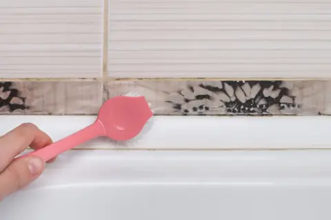 Różowa szczoteczka usuwa pleśń z fugi przy wannie. Dowiedz się, jak usunąć pleśń z plastiku i innych powierzchni.