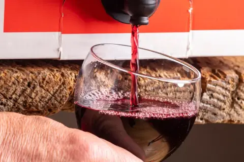 Czerwone wino leje się z kartonu do kieliszka. Wygodny sposób na serwowanie wina w 5 litrowej butelce.