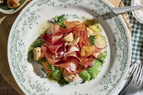 Deliziosi antipasti di terra con affettati rosa, funghi e verdure fresche su un piatto decorato.