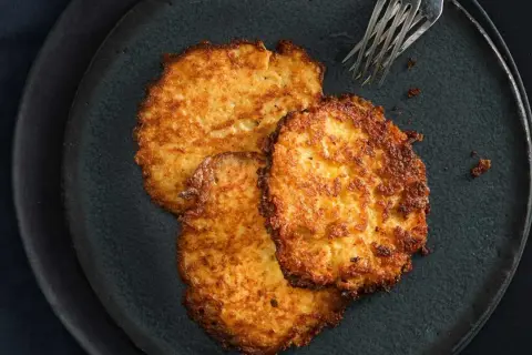 Drei goldbraune Kartoffelpuffer liegen auf einem dunklen Teller. Perfekt für den Thermomix!