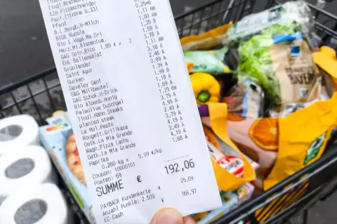 Kassenbon mit vielen Produkten, Einkaufswagen im Hintergrund. Die Digitalisierung im Handel wird durch solche Belege und die Möglichkeit zur digitalen Erfassung von Einkäufen sichtbar.