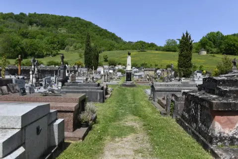Vue d'un cimetière avec des tombes et des croix, sur fond de colline verdoyante.