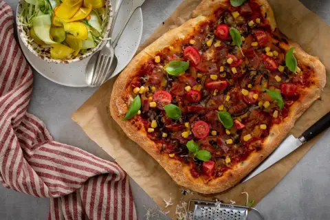 En härlig pizza med köttfärs och lök, toppad med körsbärstomater, majs och basilika. Serveras med en fräsch sallad.