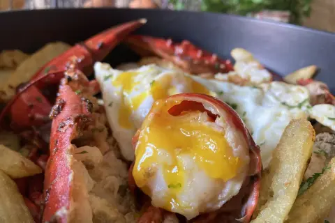 Deliciosos huevos rotos con bogavante, patatas fritas crujientes y un huevo con la yema perfecta.