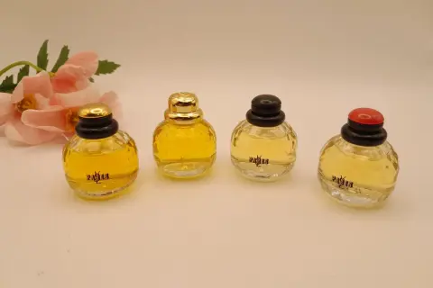 Cztery miniaturowe flakoniki perfum YSL Paris, obok delikatnych różowych kwiatów.