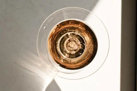 Szklanka z różowym, musującym winem dealkoholizowanym, w świetle słońca. Bąbelki unoszą się ku górze.
