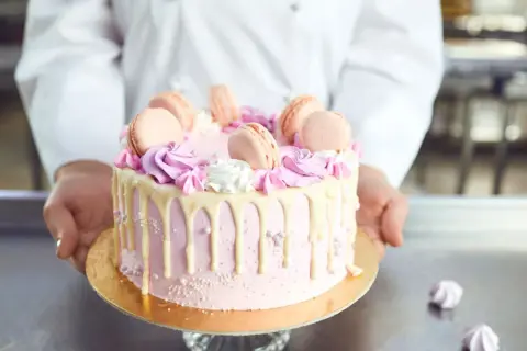 Różowy tort z makaronikami i kremem. Idealne ozdoby do tortu znajdziesz w cukierni.