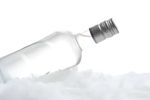 Szklana butelka wódki leży na lodzie, tworząc wrażenie, kiedy wódka zamarza.