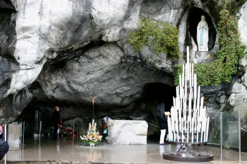 Pilger beten in der Lourdes Grotte Bernadette. Eine Marienstatue und Kerzen stehen in der Höhle.