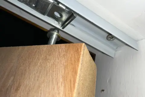 Detalle de una puerta armario descolgada, con el soporte metálico visible y el borde de madera.