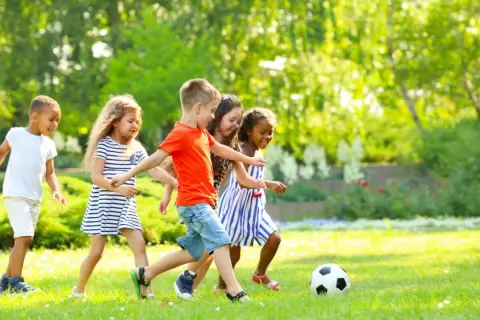 Kinder haben Spaß bei Bewegungsspielen im Kindergarten. Sie spielen Fußball auf einer sonnigen Wiese.