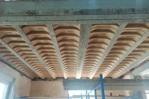 Widok od dołu na różne rodzaje stropów: betonowe belki i płyty, a także pustaki ceramiczne tworzące łuki.