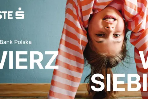 Uśmiechnięta dziewczynka w pasiastej bluzce robi mostek. Logo Erste Group i hasło "WIERZ W SIEBIE" zachęcają do wiary we własne możliwości.
