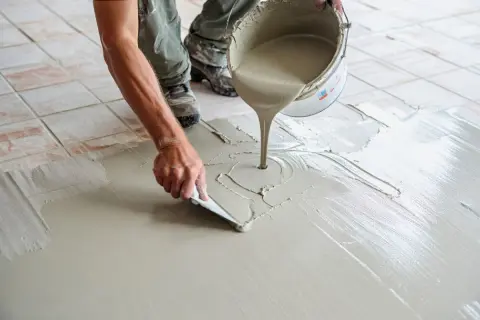 Application de béton ciré sur carrelage sol. Un ouvrier étale le produit avec une spatule, créant une surface lisse et moderne.