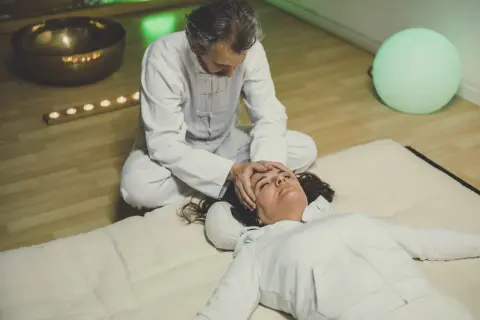 Un praticien effectue un massage japonais shiatsu sur le visage d'une femme allongée, dans une ambiance apaisante avec une lumière verte et des bougies.