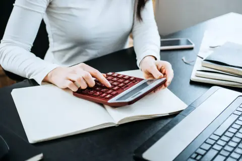 Kobieta liczy wydatki na własne cele mieszkaniowe, przygotowując PIT-39. Na biurku notatnik, kalkulator i laptop.