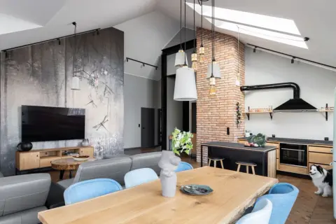 Nowoczesny styl loftowy salon z jadalnią i kuchnią. Ściana z motywem ważek, szara sofa, drewniany stół i ceglana ściana.