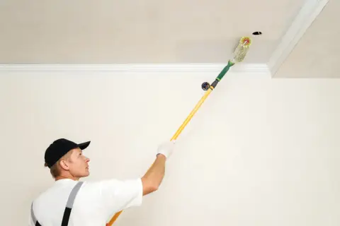 Un peintre utilise un rouleau à long manche pour peindre un plafond, suivant un schéma précis pour un résultat parfait.