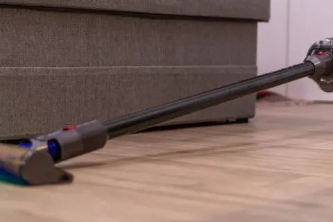 Odkurzacz Dyson na drewnianej podłodze przy meblu.