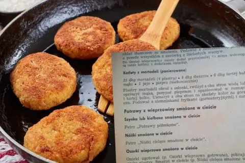 Złociste kotlety z mortadeli, usmażone na patelni, czekają na podanie z ziemniakami.