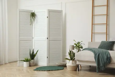 Weißer Klapp-Raumteiler mit Pflanzen und Sofa in hellem Wohnbereich.