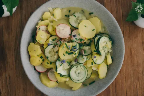 Ein Teller mit traditionellem bayrischem Kartoffelsalat, garniert mit Radieschen, Gurken und Schnittlauch.