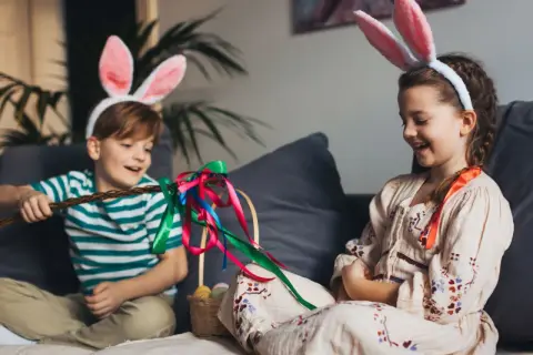 Dzieci w króliczych uszach cieszą się przerwą świąteczną wielkanocną, bawiąc się palmą i koszykiem z pisankami.