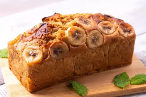 Pyszny chlebek bananowy Ani gotuje się w piekarniku. Z wierzchu ozdobiony plasterkami banana i listkami mięty.