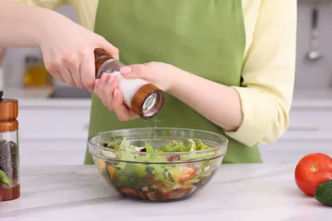 Manos sazonando una ensalada con sal, uno de los usos de la sal en la cocina.