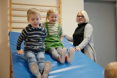 Zwei Kinder rutschen auf einer blauen Matte, während eine Erzieherin zusieht. Ein Fall könnte eine aufsichtspflichtverletzung kita darstellen.