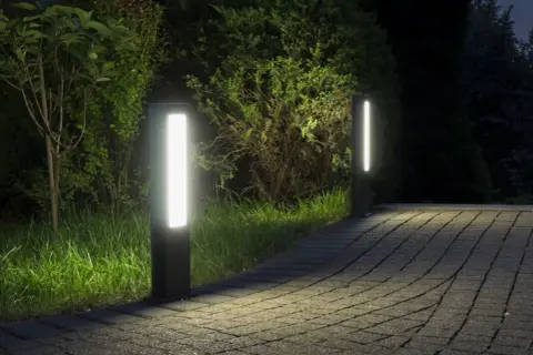 Dwa nowoczesne słupki LED oświetlają ścieżkę z kostki brukowej w ogrodzie.