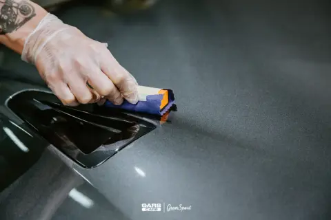 Nakładanie ceramiki lakieru na ciemnoszary element samochodu. Ręka w rękawiczce aplikuje produkt.