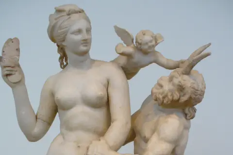 Sculpture grecque antique : Vénus, un putto ailé et un satyre. La déesse tient un objet brisé.