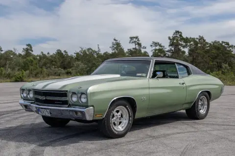 Grön Chevelle SS från 1970 med vita ränder på huven, parkerad utomhus med träd i bakgrunden.