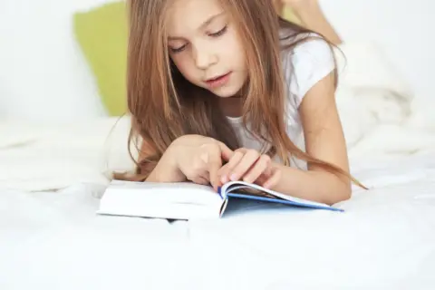 Une jeune fille de 11 ans, allongée sur un lit, est absorbée par la lecture d'un livre.