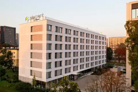 Nowoczesny hotel Element by Westin z zielonym logo na dachu, otoczony drzewami i innymi budynkami.