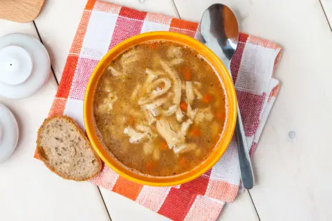 Aromaticzne flaki po zamojsku w pomarańczowej misce, obok kromka chleba i łyżka.