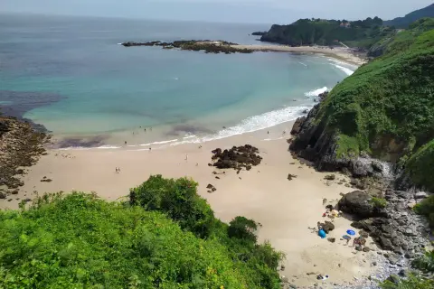 Vista aérea de la playa de Aramal, con arena dorada, aguas turquesas y gente disfrutando del sol y el mar.