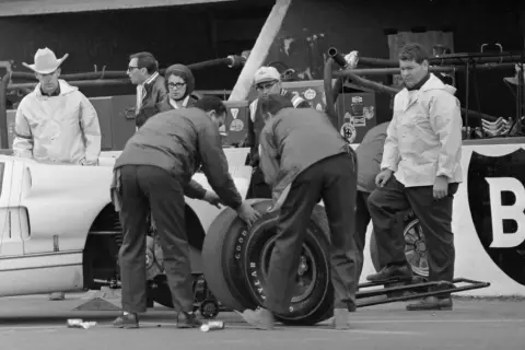 Zespół mechaników przy Fordzie GT40 podczas wyścigu Le Mans 1966. W tle widać kierowcę w kapeluszu kowbojskim.