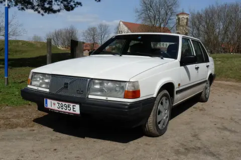 Białe Volvo 840 z przodu, na tle drzew i kościoła.