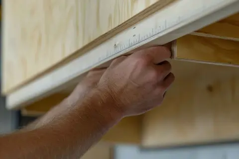 Man mid-measure, planning como poner baldas en un armario. Mide con precisión la madera para un ajuste perfecto.