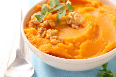 Un bol de purée de patate douce onctueuse, garni de noix croquantes et de persil frais. Un délice réconfortant.