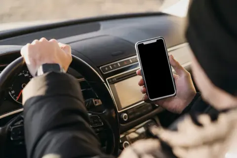 Kierowca trzyma telefon podczas jazdy, ryzykując mandat za korzystanie z telefonu.