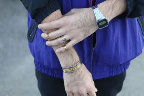 Combinaciones de pulseras y anillos dorados y plateados en brazos y muñecas, con reloj digital.